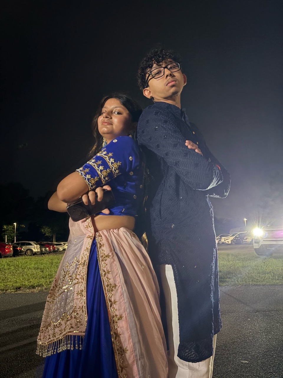 The two of us standing back-to-back with crossed arms in blue outfits at night.
